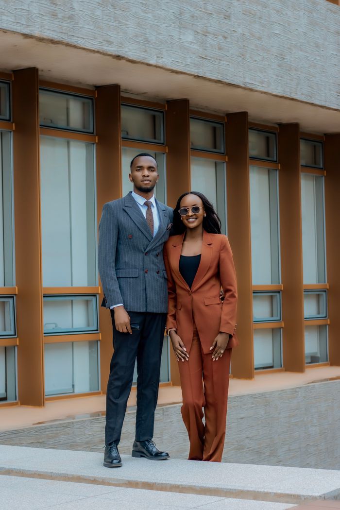 about-us Elegant man and woman in suits posing confidently with modern building backdrop.