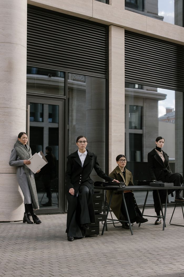 who-we-are Group of women in business attire outdoors by office building, showcasing modern style.