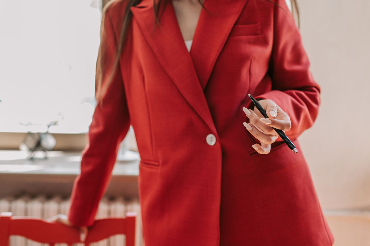 about-us Confident woman in red blazer holding a pen, ready for business leadership.